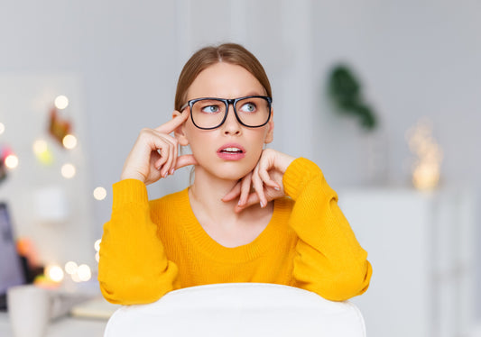 image of woman in glasses sitting at a desk in a thinking pose